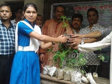 Handing a sapling to a student at a tree plantation programme
